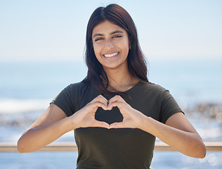 Image showing Beach portrait and heart hand woman for summer holiday freedom, happiness and wellness. Happy Indian girl enjoying sun at ocean with love shape and optimistic smile for travel adventure.