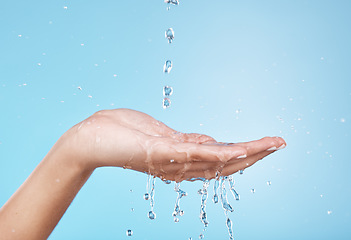 Image showing Hand, water and hydration with a woman cleaning in studio on a blue background for hygiene or personal care. Water splash, health and skincare with a female washing hands in the shower or bathroom