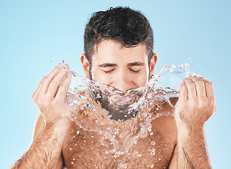 Image showing Man, splash and face for beauty in studio for wellness, health or self care cleaning by blue background. Model, bathroom and water drops with hands for healthy facial, self love and cosmetic backdrop