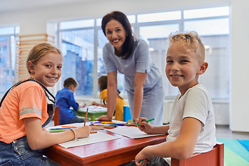 Image showing Creative kids during an art class in a daycare center or elementary school classroom drawing with female teacher.