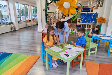 Image showing Creative kids during an art class in a daycare center or elementary school classroom drawing with female teacher.