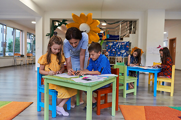 Image showing Creative kids during an art class in a daycare center or elementary school classroom drawing with female teacher.