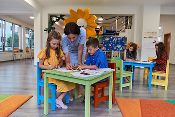 Image showing Creative kids during an art class in a daycare center or elementary school classroom drawing with female teacher.