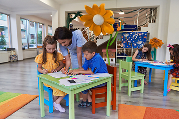 Image showing Creative kids during an art class in a daycare center or elementary school classroom drawing with female teacher.