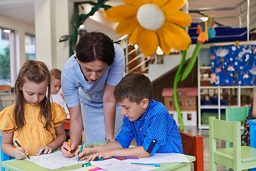 Image showing Creative kids during an art class in a daycare center or elementary school classroom drawing with female teacher.