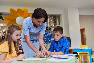 Image showing Creative kids during an art class in a daycare center or elementary school classroom drawing with female teacher.