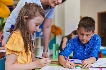 Image showing Creative kids during an art class in a daycare center or elementary school classroom drawing with female teacher.