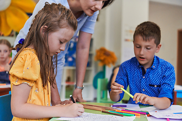 Image showing Creative kids during an art class in a daycare center or elementary school classroom drawing with female teacher.