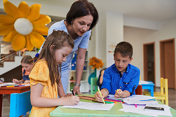 Image showing Creative kids during an art class in a daycare center or elementary school classroom drawing with female teacher.