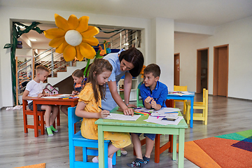 Image showing Creative kids during an art class in a daycare center or elementary school classroom drawing with female teacher.