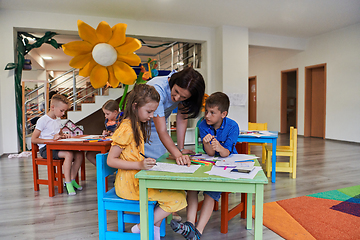 Image showing Creative kids during an art class in a daycare center or elementary school classroom drawing with female teacher.