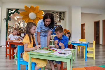 Image showing Creative kids during an art class in a daycare center or elementary school classroom drawing with female teacher.