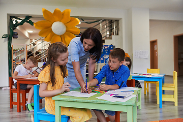 Image showing Creative kids during an art class in a daycare center or elementary school classroom drawing with female teacher.