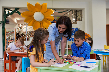 Image showing Creative kids during an art class in a daycare center or elementary school classroom drawing with female teacher.