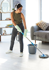 Image showing Music, cleaning and mop with woman in living room streaming while housekeeping, sanitary and hygiene. Mobile radio, podcast and listening to headphones with girl cleaner mopping floor for hospitality