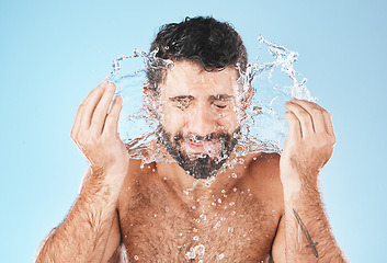 Image showing Face, splash and man in studio for cleaning, wellness and personal health with self care by blue background. Model, facial and healthy with water splash, skincare and cosmetics by studio backdrop