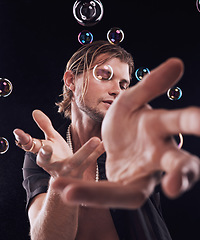 Image showing Man, hands and bubbles in studio for magic, art performance or creative show by black background. Model, artist and soap with rainbow light, dark mystery aesthetic or theater presentation by backdrop