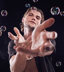 Image showing Bubbles, hands and man in studio for magic portrait, art performance and creative by black background. Alluring model, soap and rainbow light with dark mystery aesthetic or sexy show by backdrop