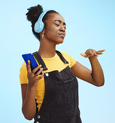 Image showing Black woman, music and phone in studio with dance, dj hand gesture and listening by blue background. Gen z girl, streaming audio or online radio on internet, happy and fashion headphones by backdrop