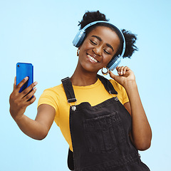 Image showing Selfie, smartphone and black woman with headphones, social media and connection on blue studio background. African American female influencer, girl and content creator with smile and online streaming