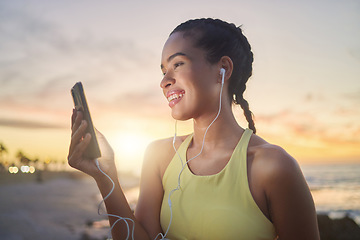 Image showing Fitness, beach and woman with smartphone after running at sunset, online and streaming music or podcast in nature for exercise. Runner, relax and scroll social media after run, smile with earphones.