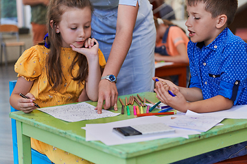 Image showing Creative kids during an art class in a daycare center or elementary school classroom drawing with female teacher.