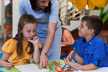 Image showing Creative kids during an art class in a daycare center or elementary school classroom drawing with female teacher.