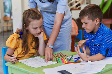 Image showing Creative kids during an art class in a daycare center or elementary school classroom drawing with female teacher.