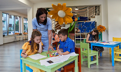 Image showing Creative kids during an art class in a daycare center or elementary school classroom drawing with female teacher.