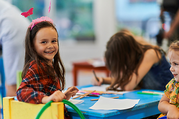 Image showing Creative kids during an art class in a daycare center or elementary school classroom drawing with female teacher.