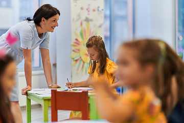 Image showing Creative kids during an art class in a daycare center or elementary school classroom drawing with female teacher.