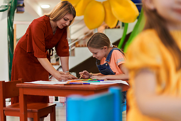 Image showing Creative kids during an art class in a daycare center or elementary school classroom drawing with female teacher.