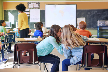 Image showing Students, friends and whispering in classroom for secret, gossip or chatting during teaching lesson. Sneaky female learners sharing quiet information secretly in ear at class while teacher is busy