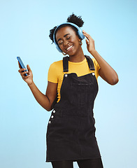 Image showing Black woman, phone and music in studio with smile, happiness or listening by blue background. Happy gen z girl, streaming audio or online radio on smartphone for edgy fashion, headphones and backdrop