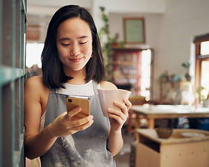 Image showing Artist woman, phone and reading chat with coffee, smile and focus on email, app or social media for date. Asian art entrepreneur, social network and smartphone with happiness, tea and relax in studio