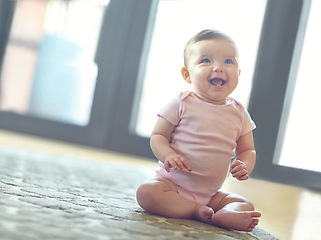 Image showing Happy, cute and adorable baby girl in her home with a smile sitting and playing on the floor. Happiness, child development and excited beautiful infant child learning to crawl in a room at the house.