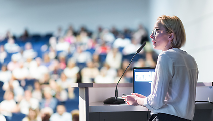 Image showing Female speaker giving a talk on corporate business conference. Unrecognizable people in audience at conference hall. Business and Entrepreneurship event.