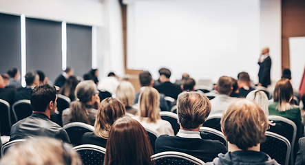 Image showing Speaker giving a talk in conference hall at business event. Rear view of unrecognizable people in audience at the conference hall. Business and entrepreneurship concept.