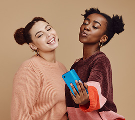 Image showing Selfie, friends and women with smartphone, social media and connection on brown studio background. Females, girls and cellphone to share photos, posting and bonding together casual, trendy and smile