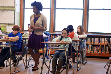 Image showing Kids, classroom and teacher woman at school, focus and education for development, learning and future. School kids, black woman and studying at table in class, diversity and notebook for writing test