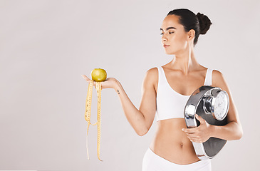 Image showing Fitness, health and woman with scale and apple for weightloss, diet and nutrition on white studio background. Exercise, wellness and girl with fruit, balance and measuring tape for healthy lifestyle