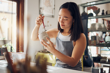 Image showing Pottery, art and design with an asian woman in a studio for her creative ceramics hobby as an artisan. Manufacturing, pattern and artist with a female potter sitting in her workshop as a sculptor