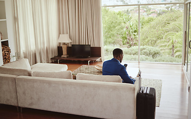 Image showing Phone, travel and hospitality with a business black man sitting on a sofa in the living room of a hotel with his luggage. Back, bag and communication with a male employee typing a text message