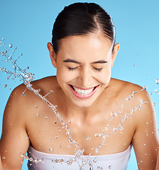 Image showing Face wash, skincare and woman isolated on blue background for beauty, cosmetics cleaning and happy. Smile of a person or model with water splash for dermatology wellness and aesthetic in studio