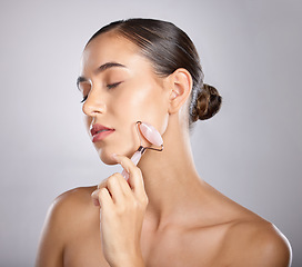 Image showing Rose quartz, face roller and woman skincare of a model relax from facial spa treatment. Isolated, studio background and young person busy with dermatology, self care and beauty treatment for skin