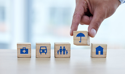 Image showing Hands, wooden blocks and building on table for essential fundamentals or safe foundation lifestyle. Hand of person putting small wood block, object or icons together of umbrella to build row on desk
