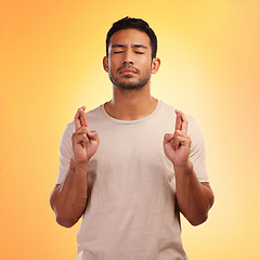 Image showing Fingers crossed, wish and man model with orange studio background and hope. Optimism, eyes closed and modern person with a beard hoping for good luck of a young casual male with a tshirt isolated