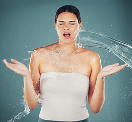 Image showing Cleaning, grooming and woman surprised with a water splash isolated on a blue background in a studio. Spa, shower and shocked girl with water for skincare, hydration and dermatology on a backdrop