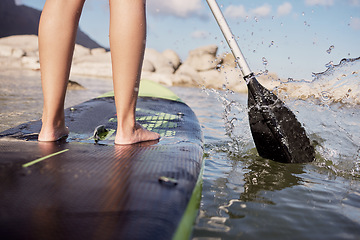 Image showing Feet, paddle surf and water with a sports woman standing on a paddle board in the sea, ocean or a river outdoor. Back, balance and sport with a female athlete outside for fitness, exercise or hobby