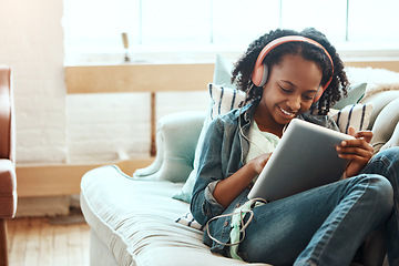 Image showing Headphones, tablet and woman on the sofa to relax while listening to music, radio or podcast. Rest, technology and African lady watching a video or movie on mobile device in her living room at home.